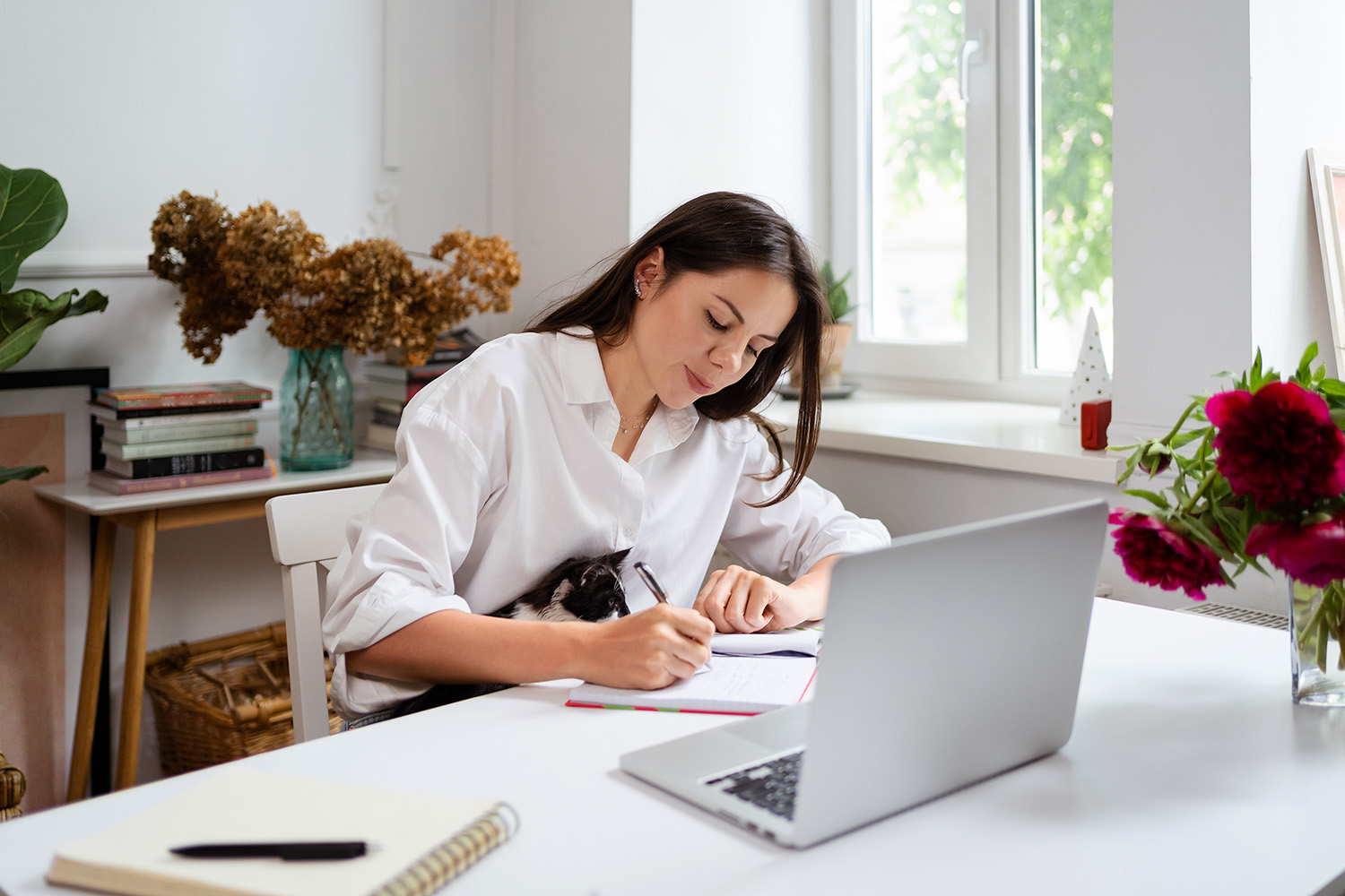 Mujer sentada en su escritorio con su laptop tomando notas en una libreta
